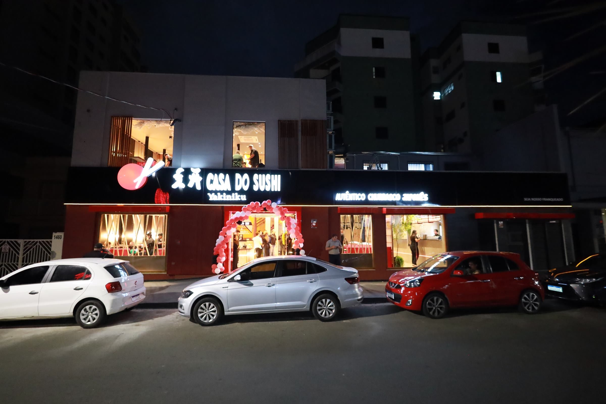 Fachada noturna do restaurante com letreiro iluminado e carros estacionados na rua em frente