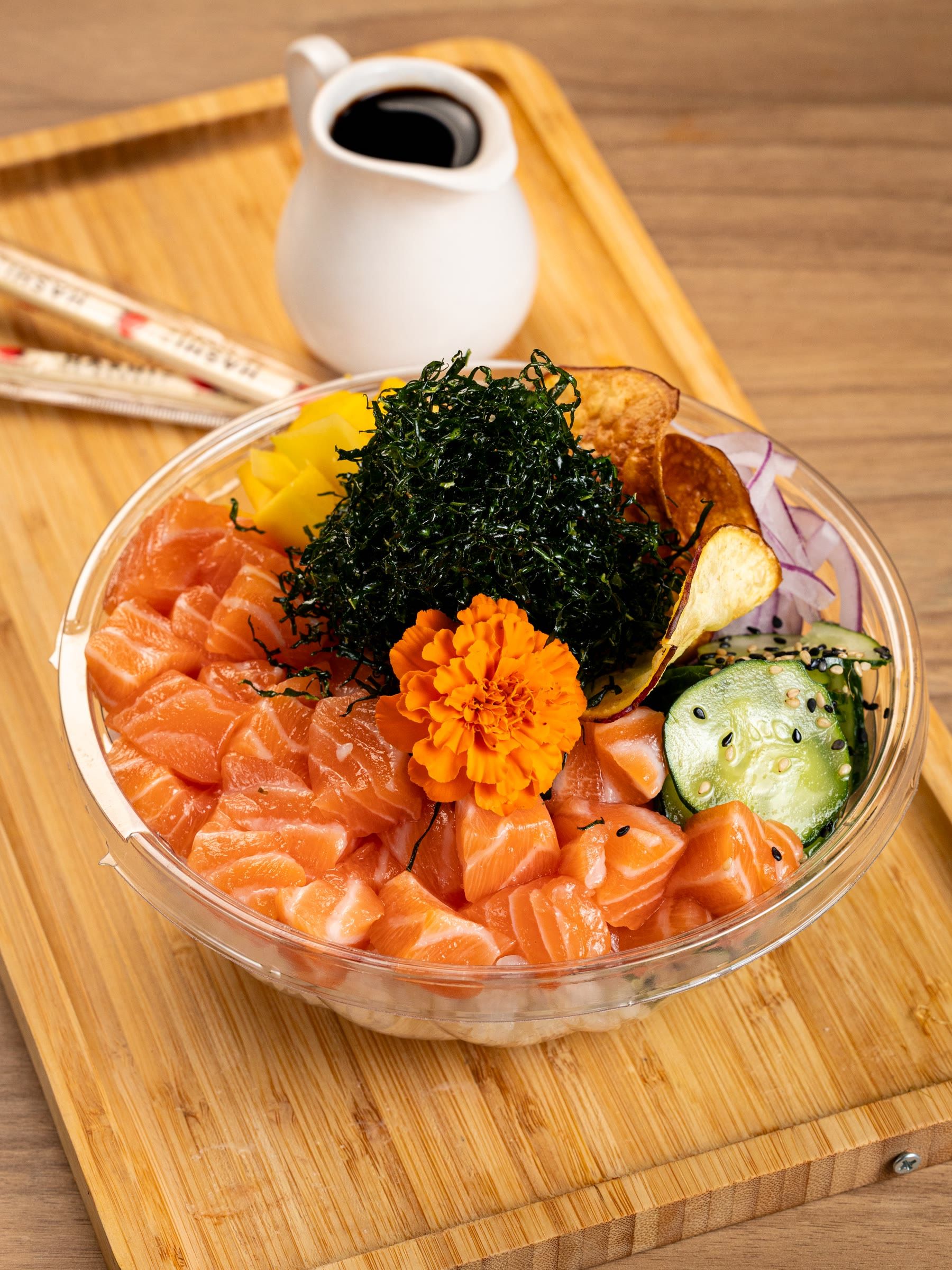 Poke farto de salmão cru alaranjado com nori, manga e flor comestível, bowl em tábua de bambu