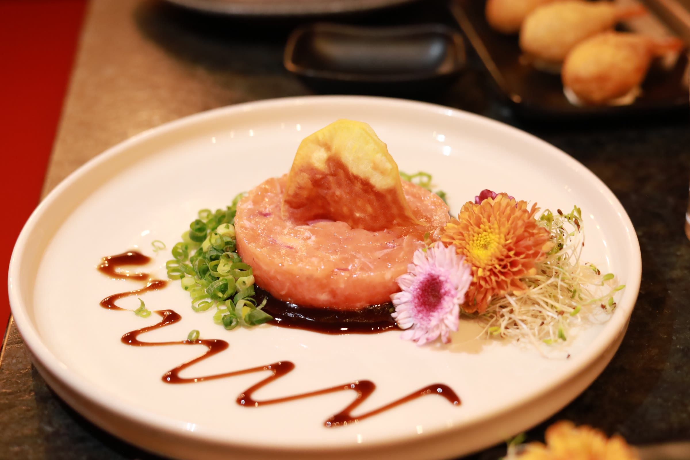 Tartar de salmao em anel com tempura dourada por cima, flores comestiveis e risco de molho em prato branco