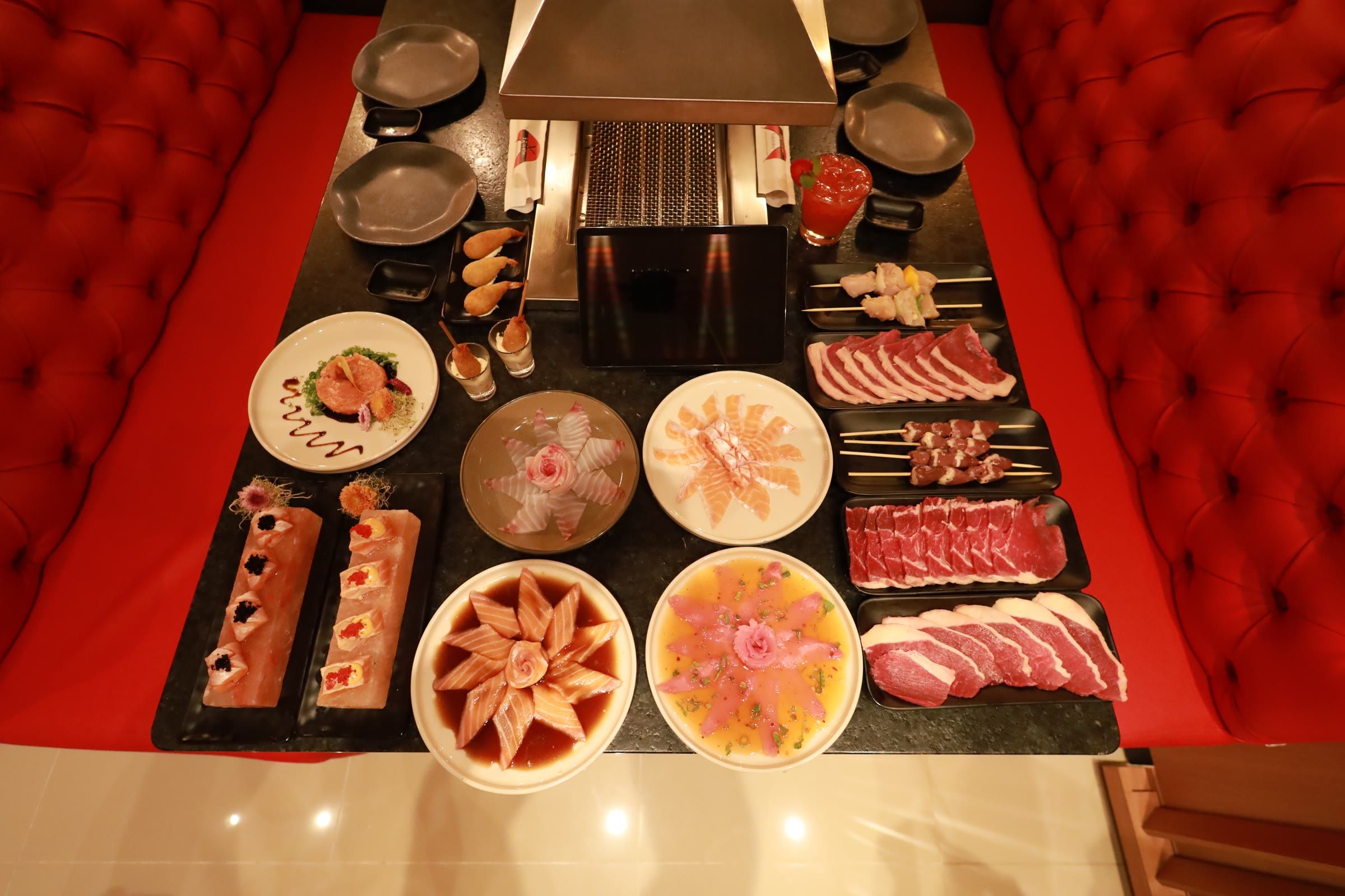 Vista de cima da mesa com sushis, carpaccios e bandejas de carne ao redor da grelha central