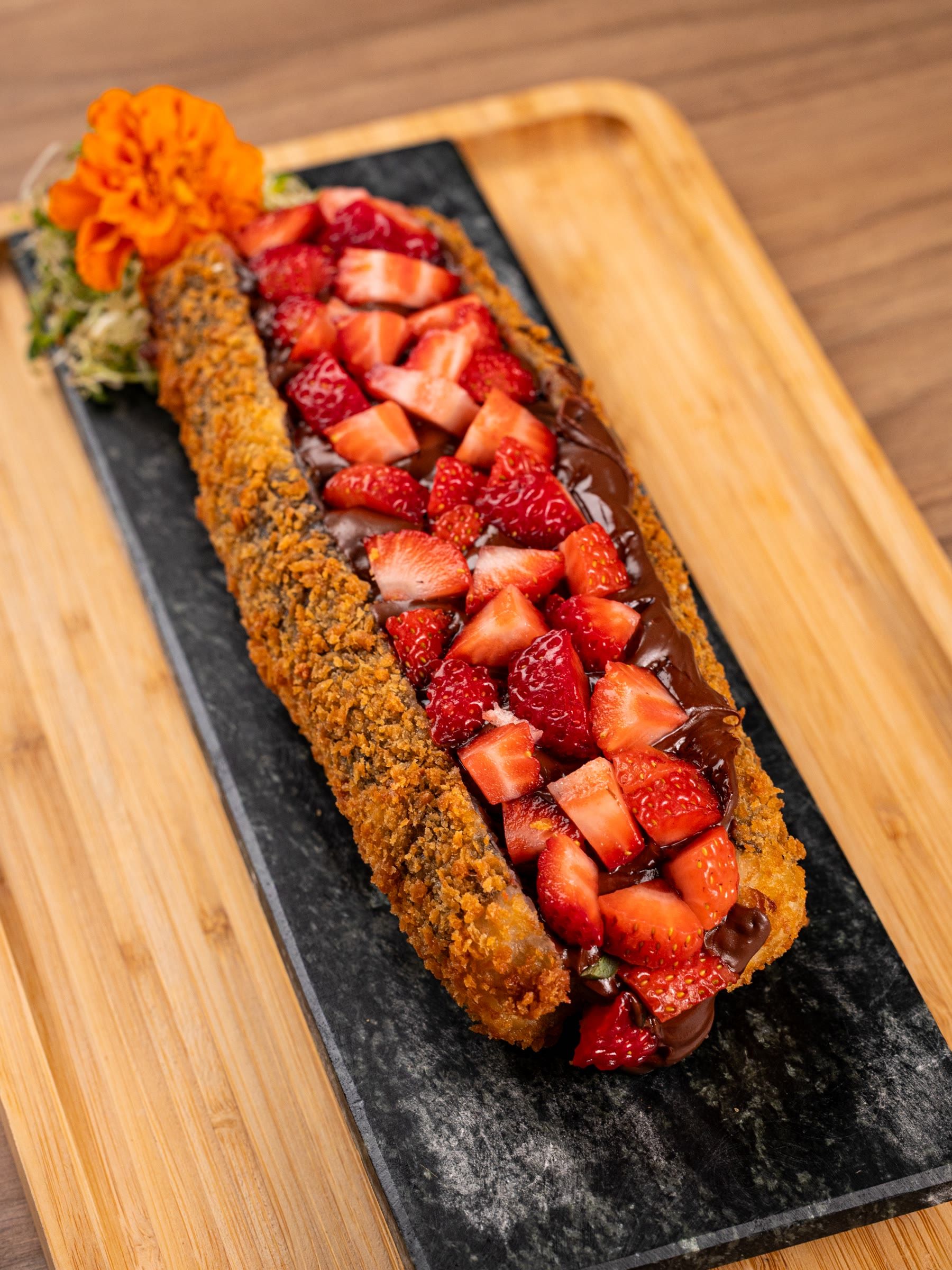 Hot roll doce comprido com morangos picados e creme branco, flor laranja na ponta da ardósia
