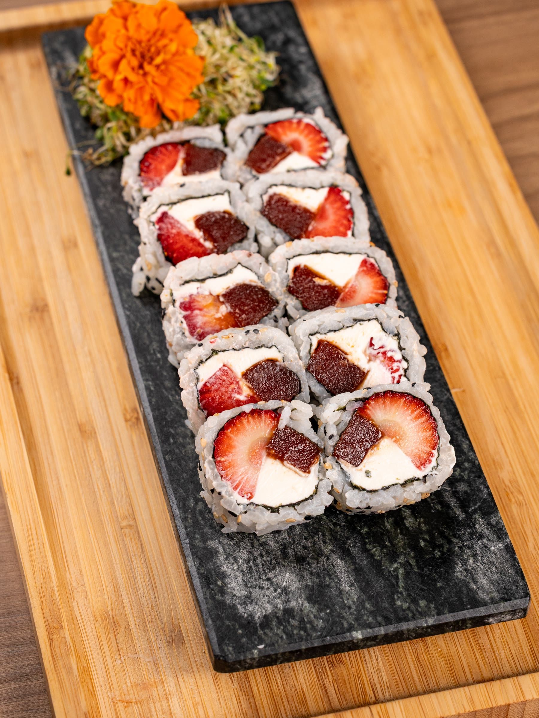 Duas fileiras de uramaki com cream cheese, goiabada e morango fatiado sobre ardosia preta