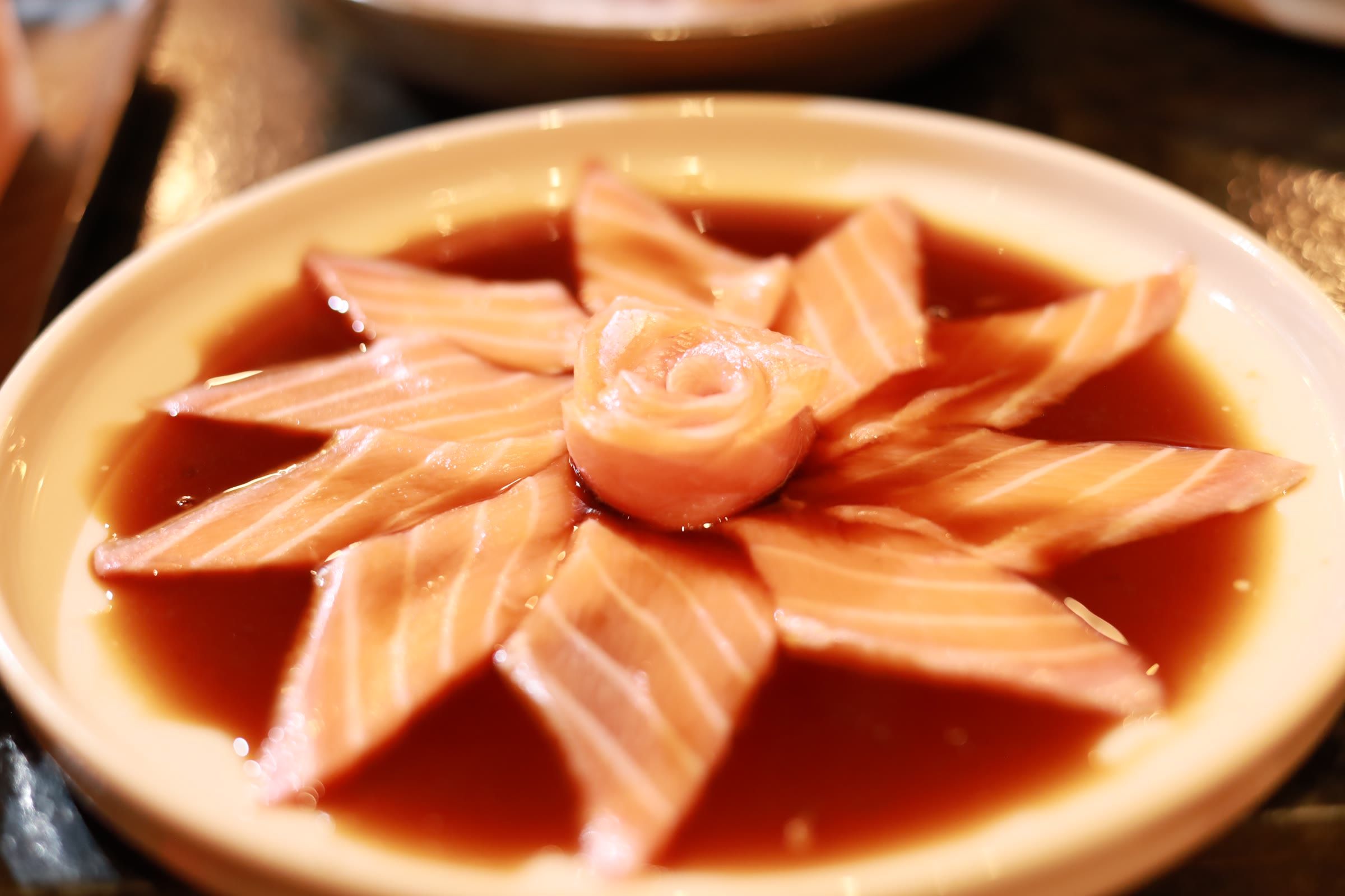 Sashimi de salmao arranjado em flor sobre molho shoyu escuro, com rosa de peixe no centro