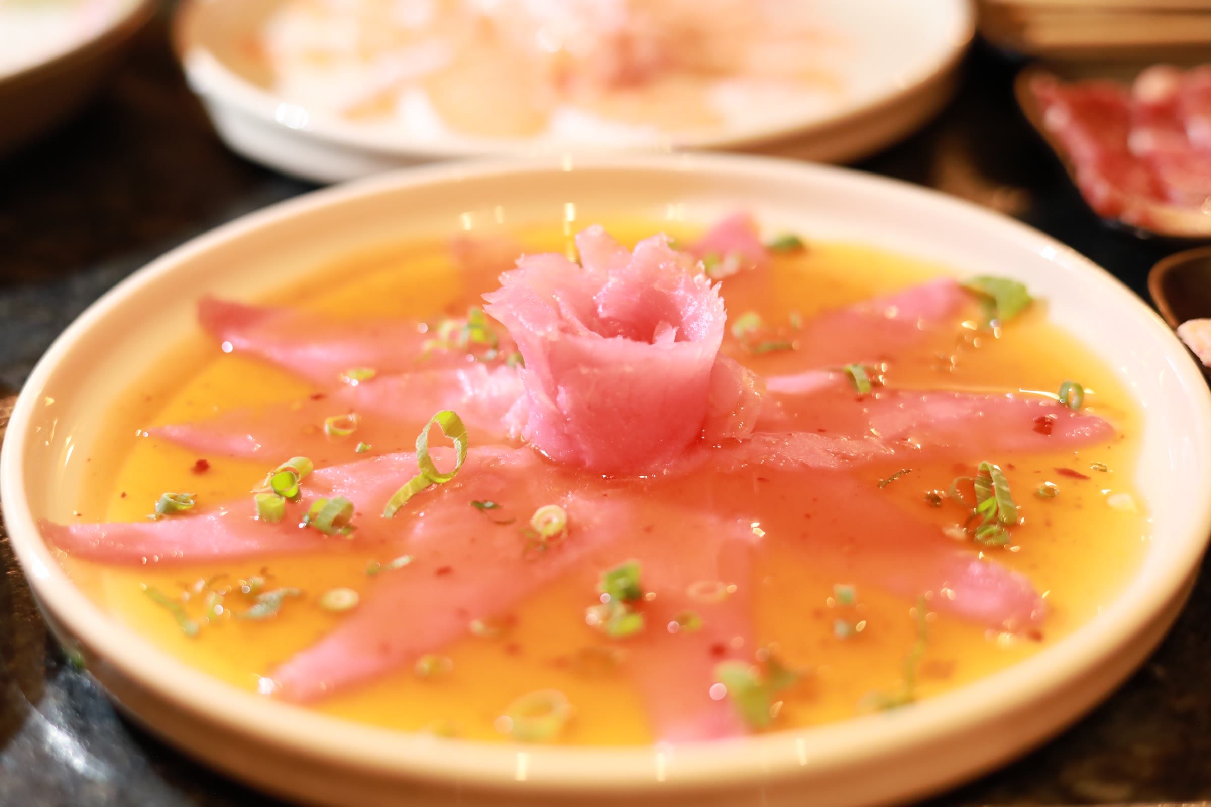 Carpaccio de salmao com molho alaranjado, cebolinha e rosa de peixe ao centro do prato