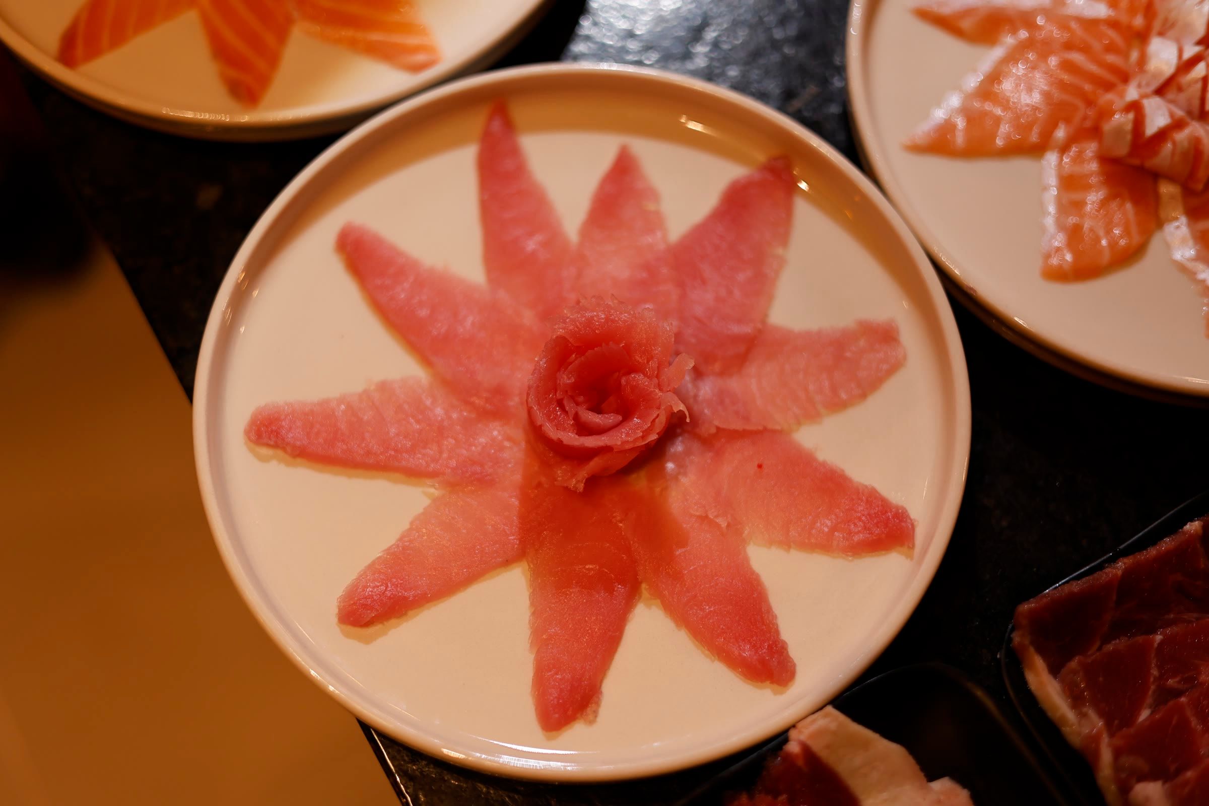 Vista de cima de três pratos de sashimi de peixe branco e salmão no balcão.