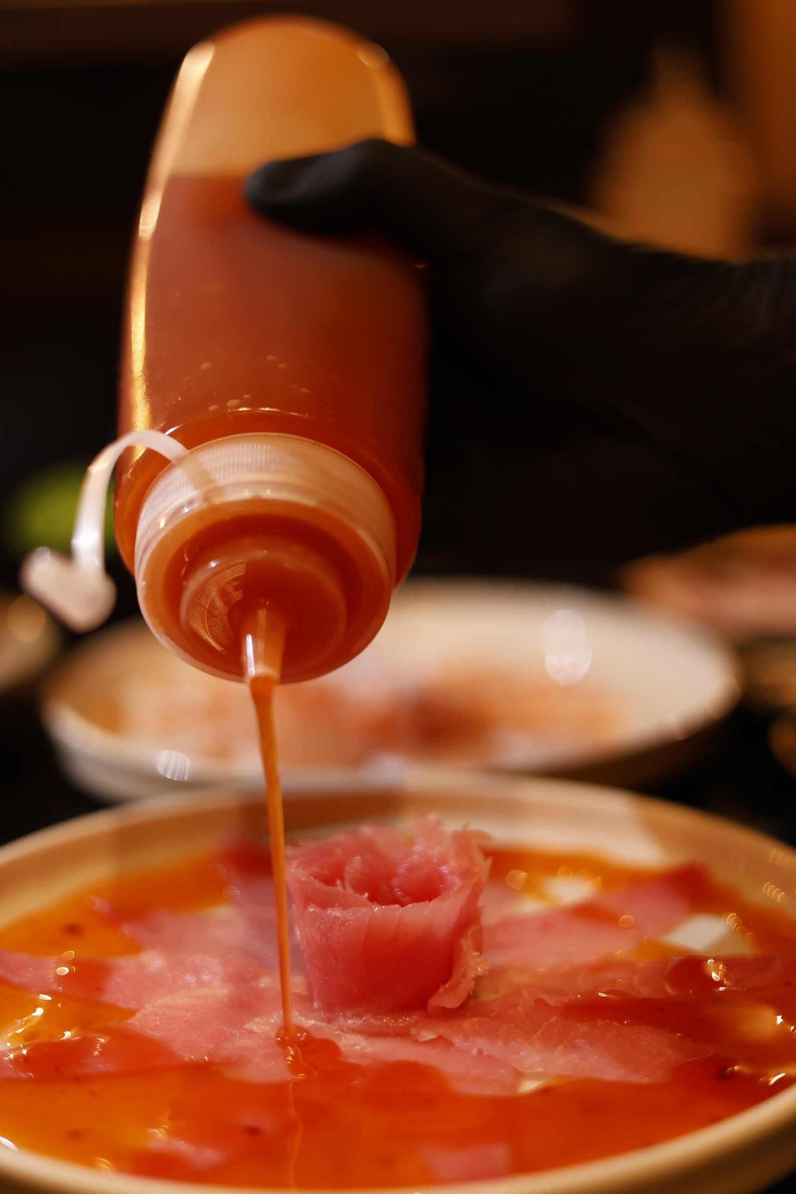 Filete de molho alaranjado cai da bisnaga direto na rosa de peixe cru do prato.