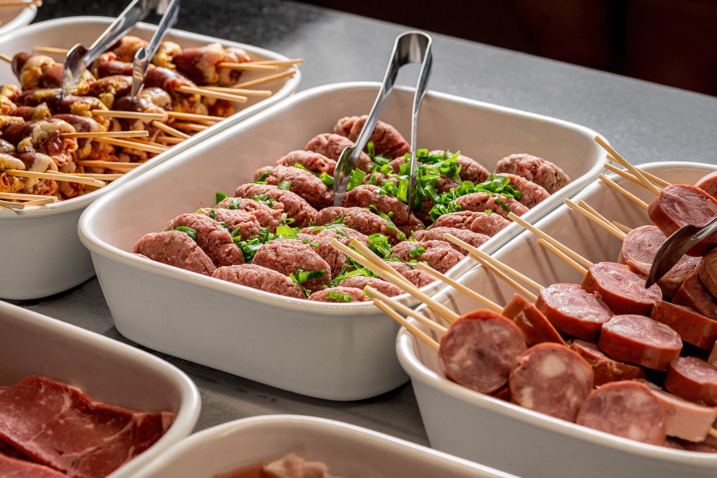 Cubas de espetinhos, kafta com ervilha e rodelas de linguica calabresa sobre o balcao de grelhar